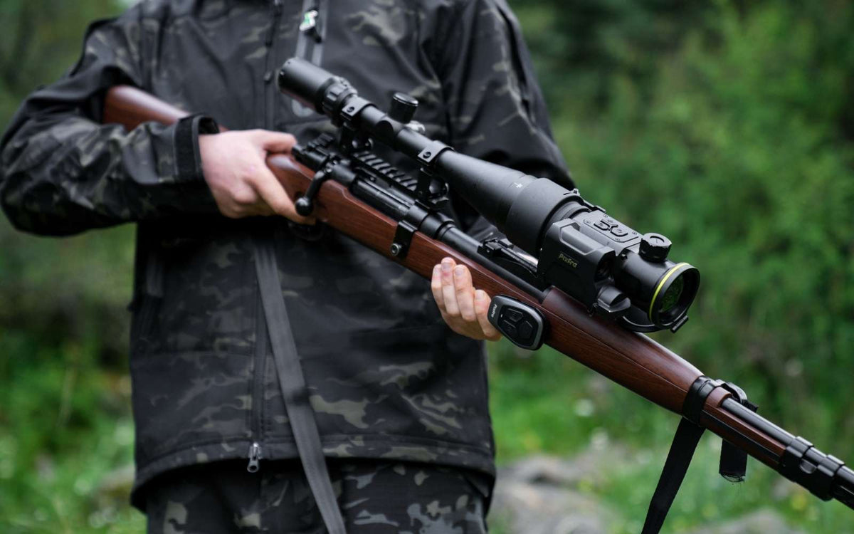Chasseur en tenue camouflage tenant sa carabine équipée du clip-on thermique Pixfra Taurus et de sa télécommande sans fil